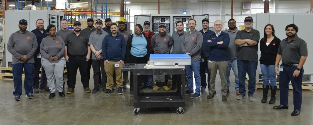 A group photo of the Kinetyc team standing together in a manufacturing facility, showcasing a diverse team of employees.