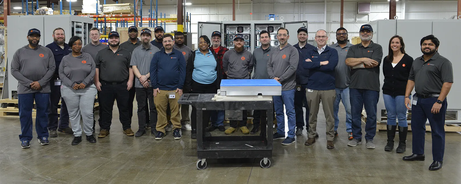 A group photo of the Kinetyc team standing together in a manufacturing facility, showcasing a diverse team of employees.