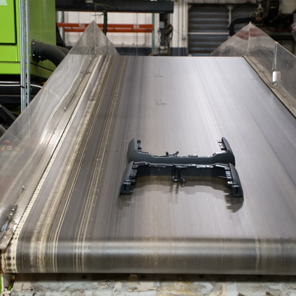 Injection molded plastic part on a conveyor belt in a manufacturing facility.
