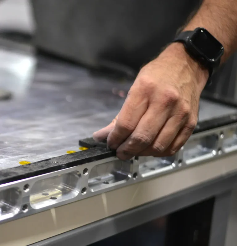 A worker's hand assembling a metal component on a workbench, demonstrating precision in manual assembly.
