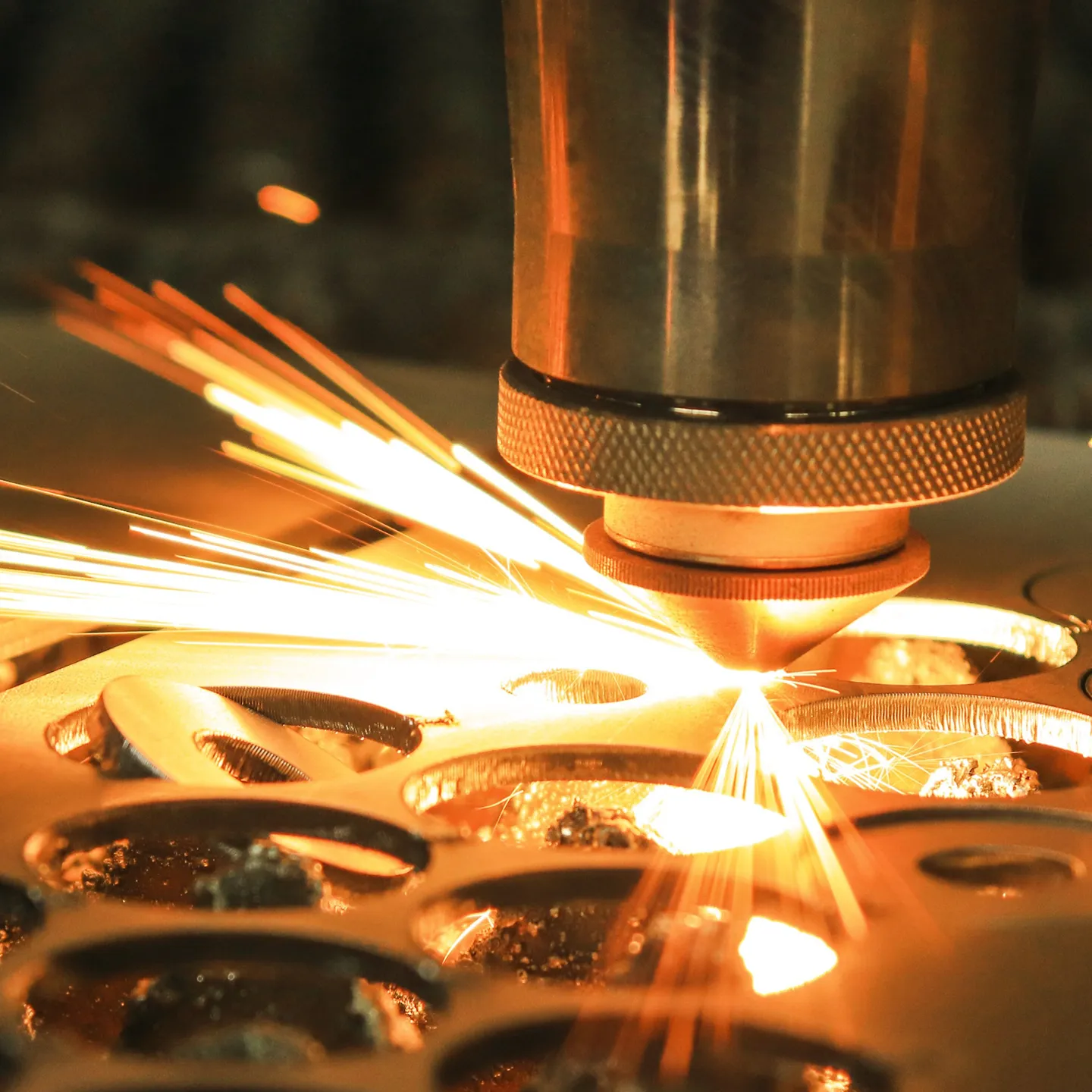 Close-up of a laser cutting machine in action, generating sparks while cutting precise shapes into a metal sheet.