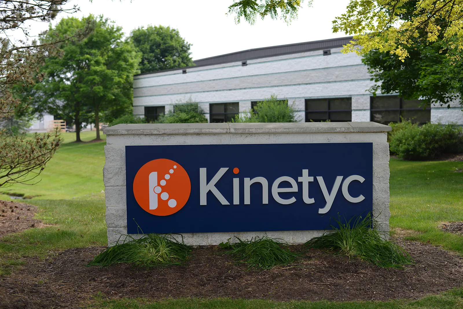 Kinetyc facility sign in front of the Wixom, Michigan headquarters, surrounded by green trees and landscaping.