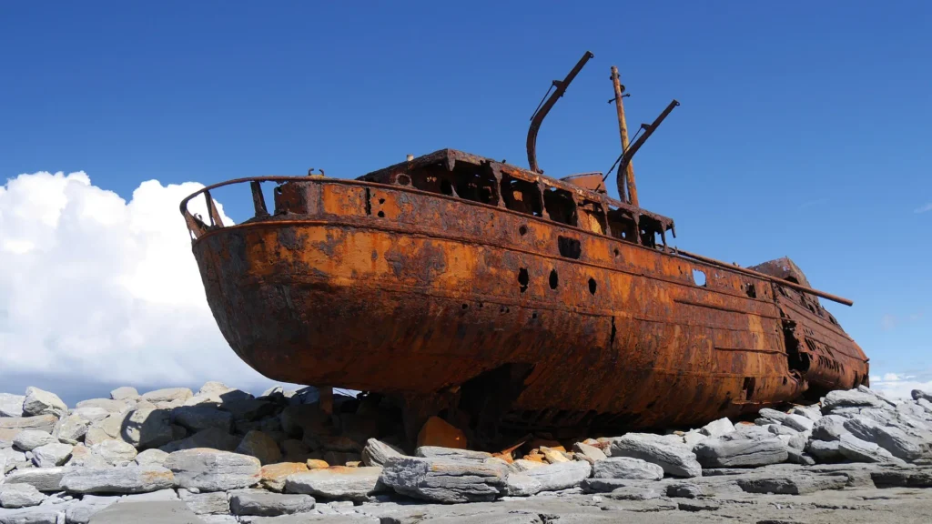 Rusting shipwreck stranded on rocky shore under a clear blue sky, symbolizing the decline of outdated offshoring practices.