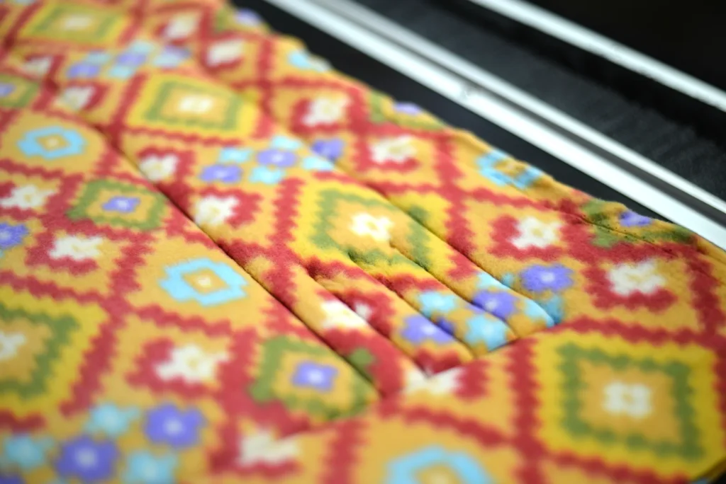 Close-up of colorful fleece fabric being laser cut at Kinetyc for Fleece & Thank You blankets and gloves, showing precision manufacturing and zero-waste innovation.