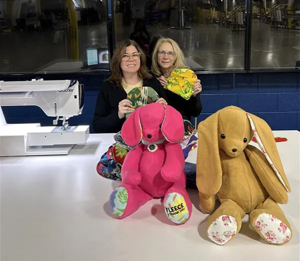 Two Kinetyc team members smiling beside handmade fleece stuffed animals created from Fleece & Thank You blanket scraps, showcasing adaptive manufacturing and zero-waste innovation.