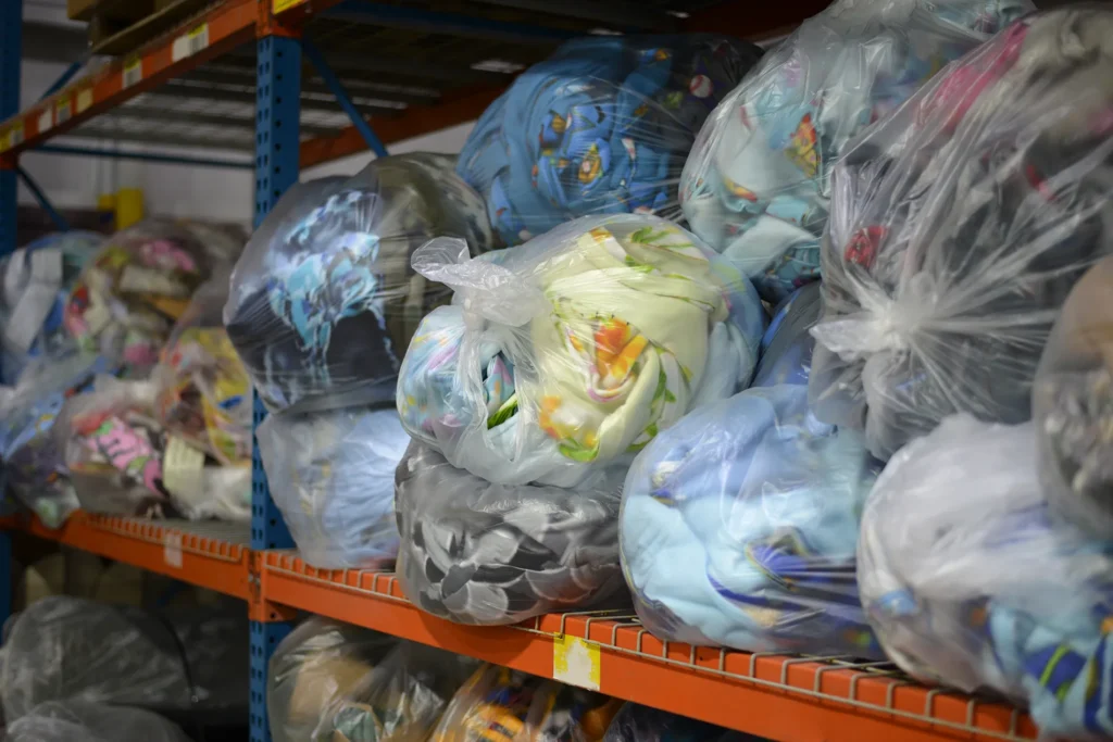 Bags of colorful fleece scraps stored on shelving at Kinetyc before being repurposed into Fleece & Thank You blankets, hats, and stuffed animals.