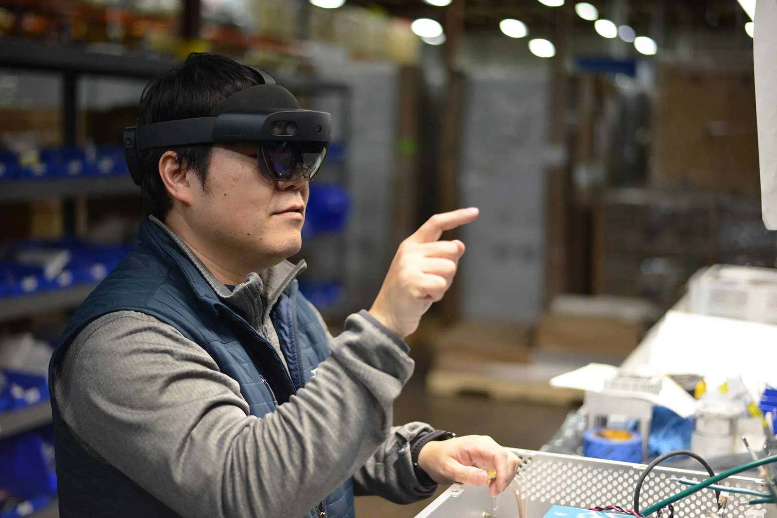Manufacturing technician using augmented reality smart glasses to assemble components on a production line.