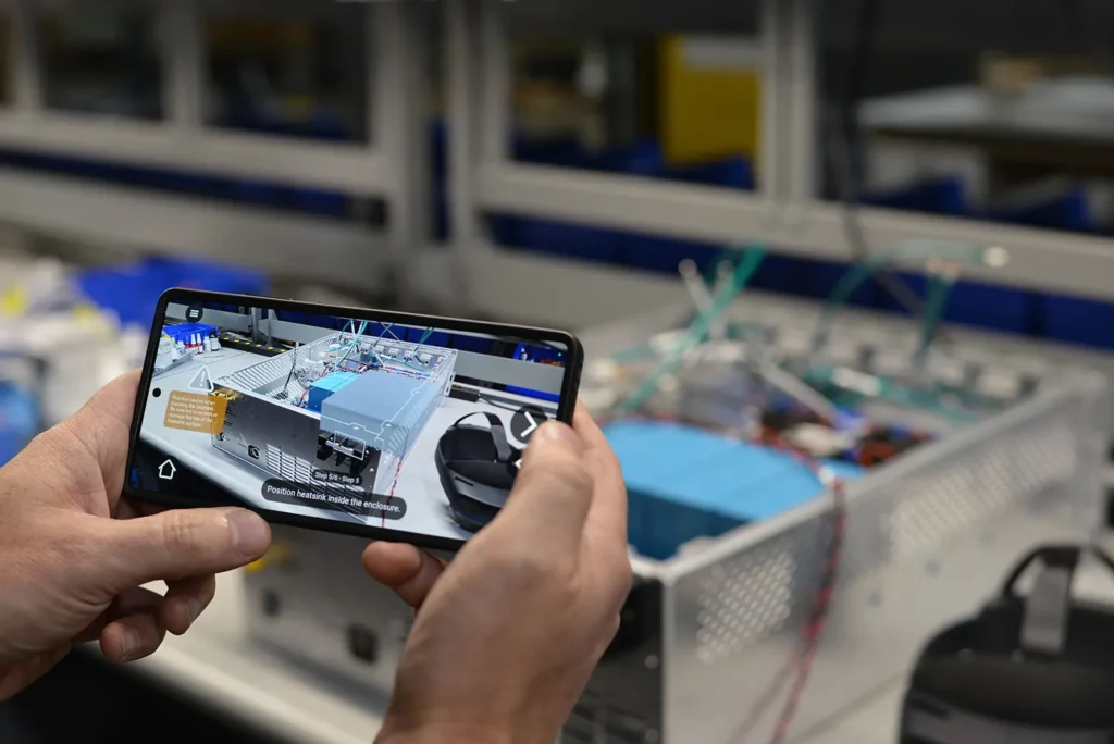 Smartphone displaying augmented reality instructions to assist with electronic assembly on a production line.