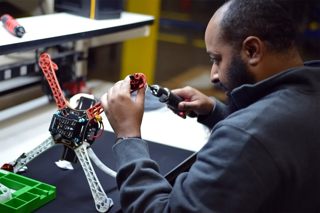 Technician assembling drone frame with electric screwdriver on workbench.