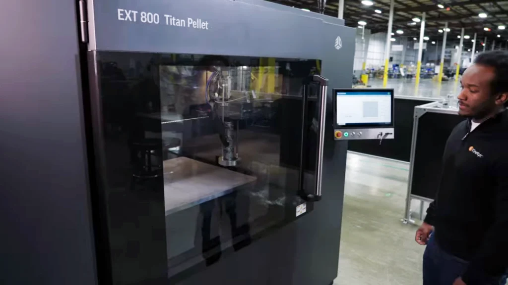 Operator monitoring Kinetyc's EXT 800 Titan Pellet 3D printer during large-format additive manufacturing production.