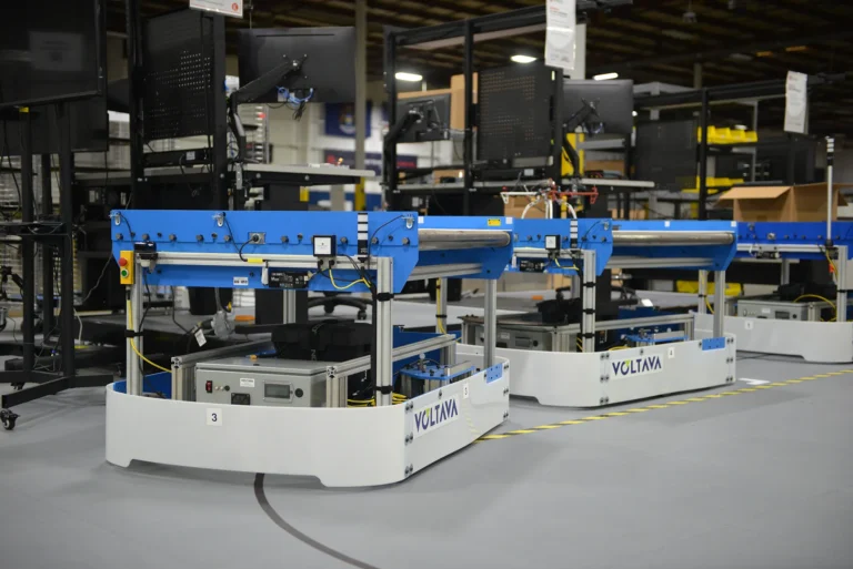 Row of blue conveyor-equipped carts beside FLEXembly assembly workstations at Kinetyc.